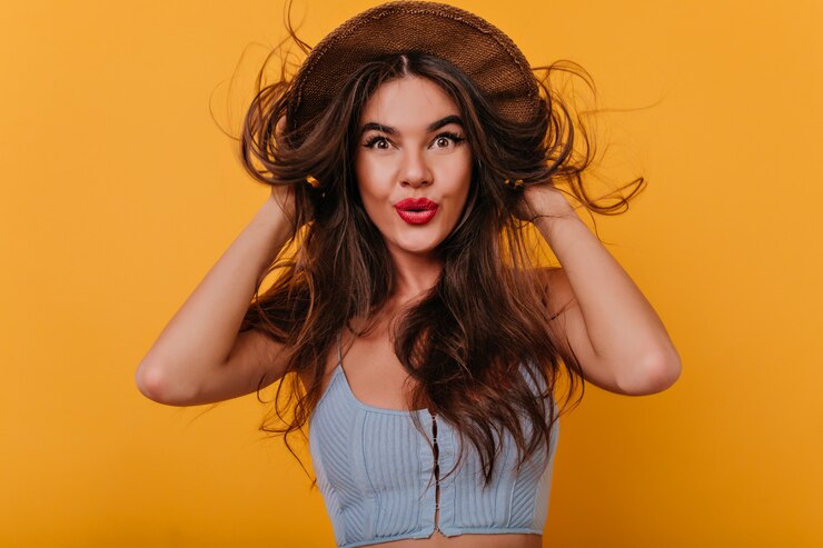 Foto gratuito encantadora dama europea con cabello largo brillante tocando su sombrero mientras posa con una sonrisa