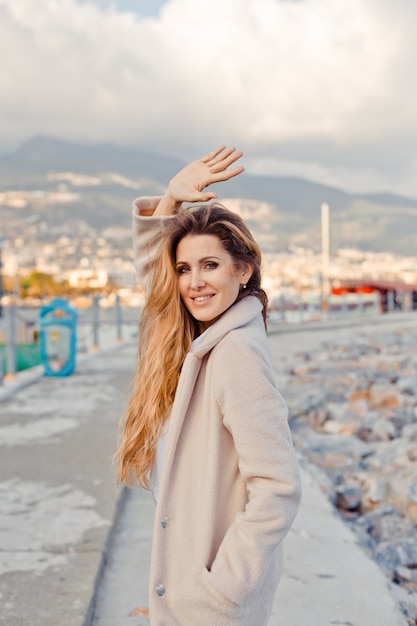 Encantadora dama de pie y agitando la mano en la playa durante el día