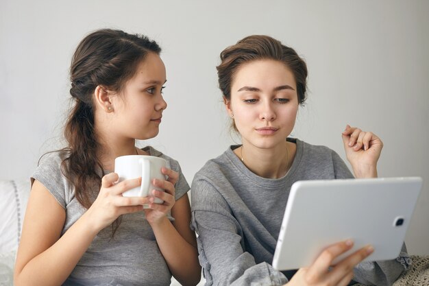 Encantadora dama tomando selfie con su hermana pequeña con tableta digital.