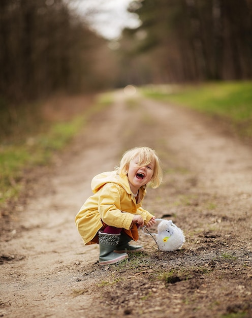 Foto gratuita encantadora y divertida niña holandesa en un abrigo impermeable amarillo y botas jugando en el campo de la campiña