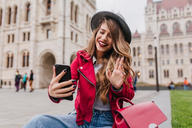 Encantadora estudiante internacional haciendo selfie frente al hermoso edificio antiguo