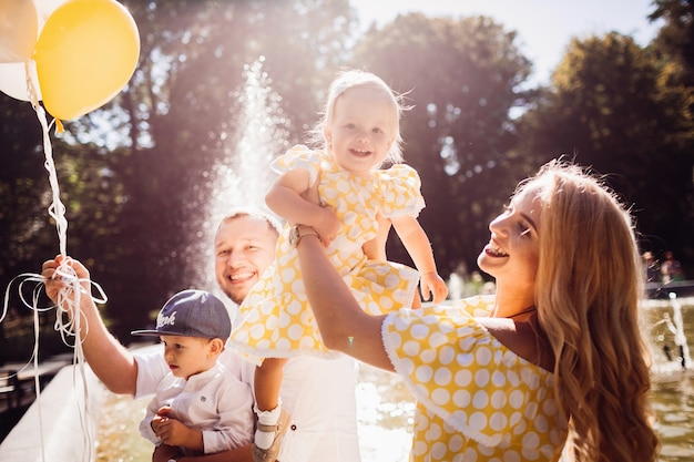 Encantadora familia vestida con la misma ropa sentada en la fuente con sus hijos y globos amarillos