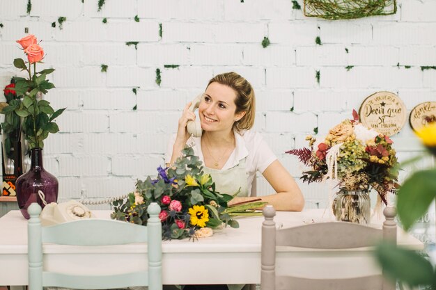 Encantadora floristería hablando por teléfono en la mesa