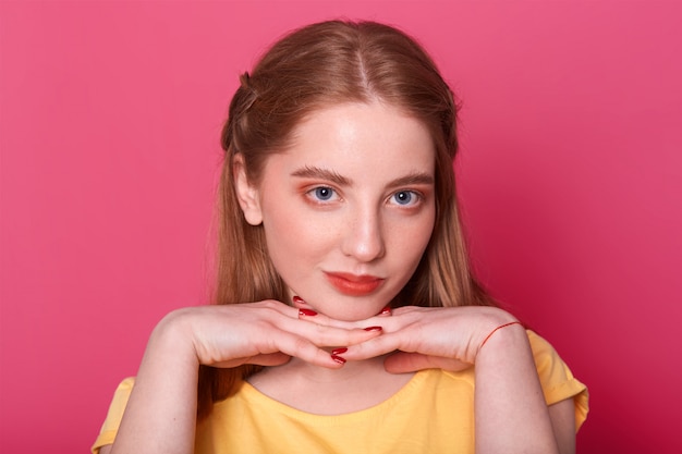 Encantadora joven adolescente, vestida con una camiseta amarilla informal, tomados de la mano bajo la barbilla, pensando en algo importante. Mujer con cabello largo y liso