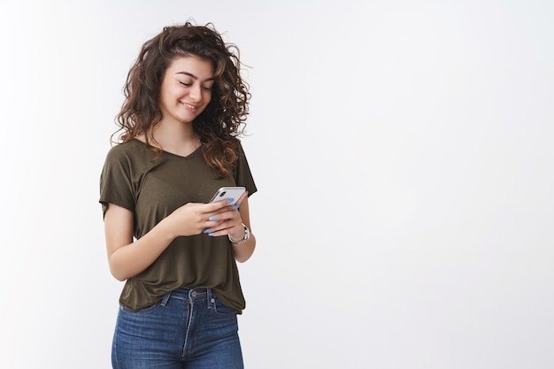 Encantadora joven armenia feliz linda mujer de pelo rizado con teléfono inteligente sonriendo suavemente riendo mensajes de texto con mensajes conmovedores divertidos, amigos chateando hacer publicación en línea actualización de perfil personal