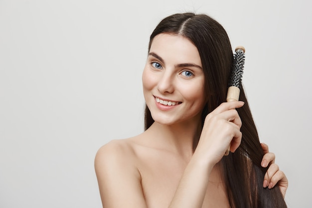 Encantadora joven cepillarse el cabello y sonriendo