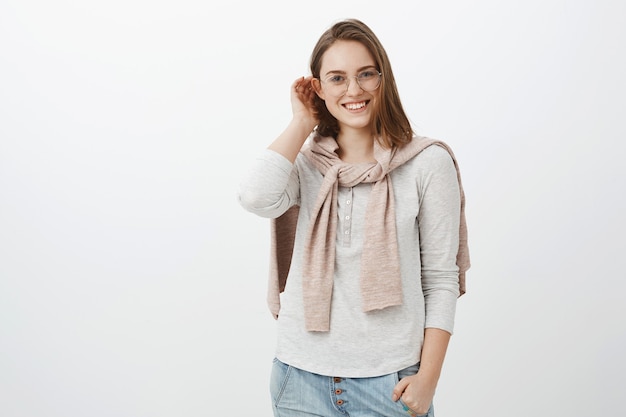 Encantadora joven morena mujer inteligente en lindos anteojos y suéter atado sobre el cuello caminando por el parque reunión chico agradable hablando casualmente sonriendo ampliamente moviendo el cabello detrás de la oreja tímido