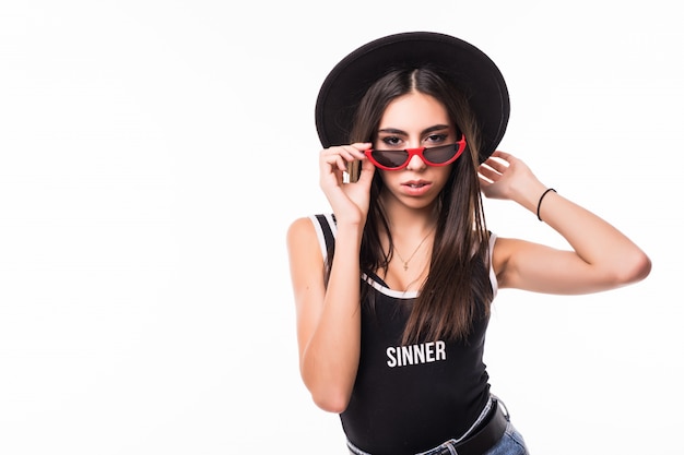 Encantadora joven morena te está mirando desde debajo de las divertidas gafas de sol