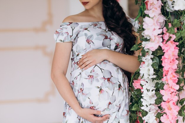 Encantadora joven mujer embarazada posa en un estudio con flores rosadas