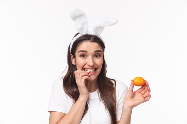 Encantadora joven en orejas de conejo sosteniendo huevo coloreado