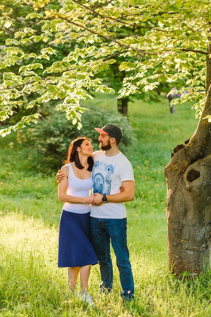 Encantadora joven pareja romántica de pie sobre la hierba verde bajo el árbol