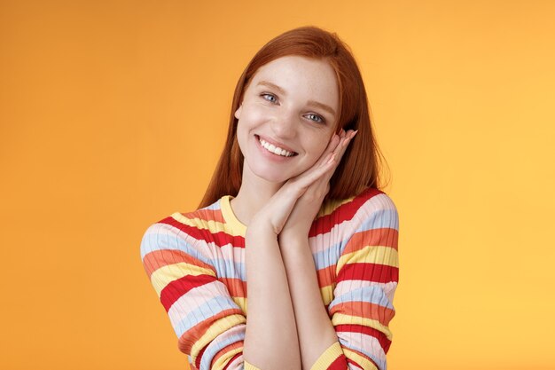 Encantadora joven pelirroja coqueta chica europea sonriendo ampliamente emocionada feliz palmera magra recibe dulce tierno presente mirada agradecida divertida reaccionando alegremente momento agradable, de pie fondo naranja.