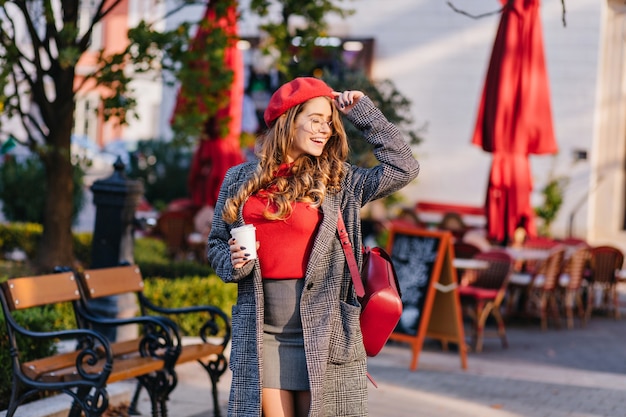 Encantadora modelo femenina en mini falda posando con los ojos cerrados en un día soleado en la calle cerca de la cafetería