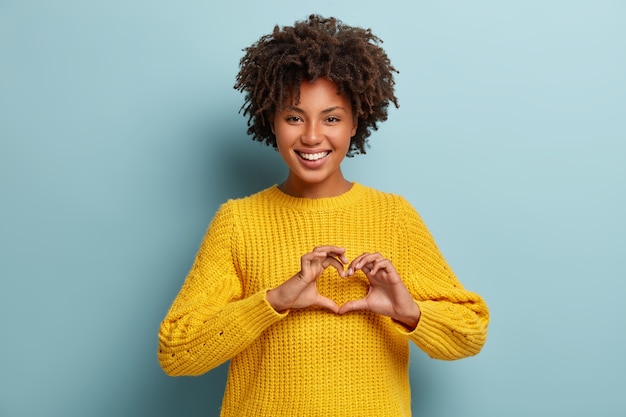 Encantadora mujer con un afro posando con un suéter rosa