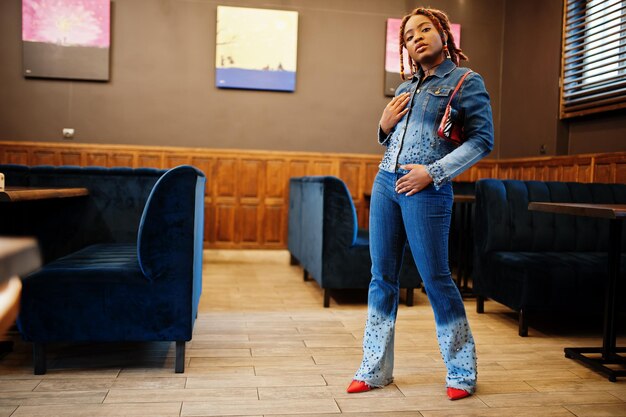 Encantadora mujer afroamericana con rastas en chaqueta de jeans con estilo azul en el café