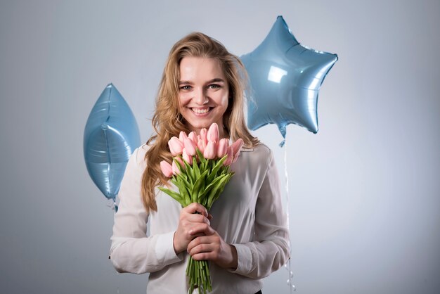 Encantadora mujer alegre con ramo de flores y globos.