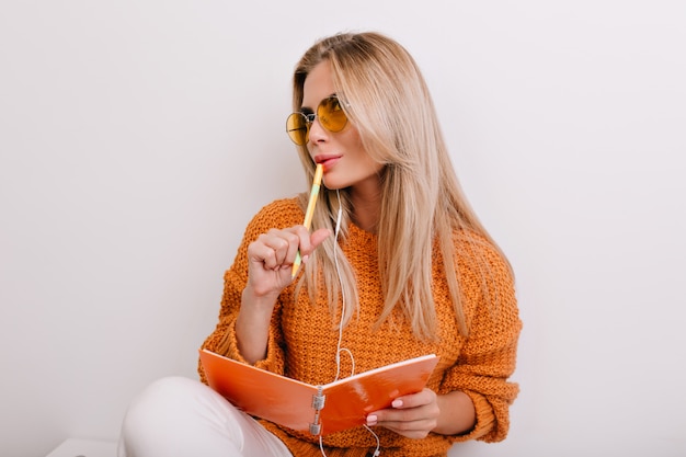 Encantadora mujer blanca escribiendo poesía en un colorido cuaderno y pensando en rimas