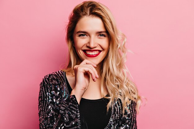 Encantadora mujer caucásica con cabello rubio riendo. Retrato de interior de una impresionante chica caucásica con labios rojos.