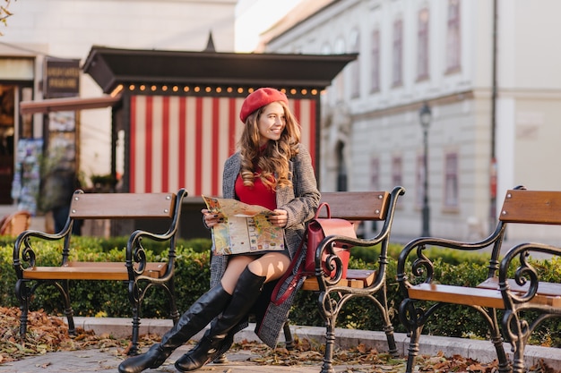 Encantadora mujer caucásica en zapatos hasta la rodilla sentado en el parque con mapa de la ciudad