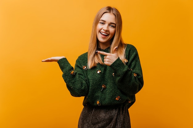 Encantadora mujer ciega en suéter de punto de moda que expresa felicidad. Retrato interior de una encantadora mujer europea de pie en naranja.