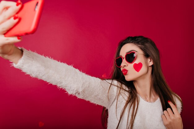 Encantadora mujer con corazón en la mejilla posando con expresión facial besos