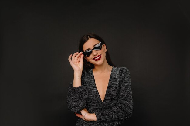 Encantadora mujer elegante con labios rojos sosteniendo sus gafas y sonrisas