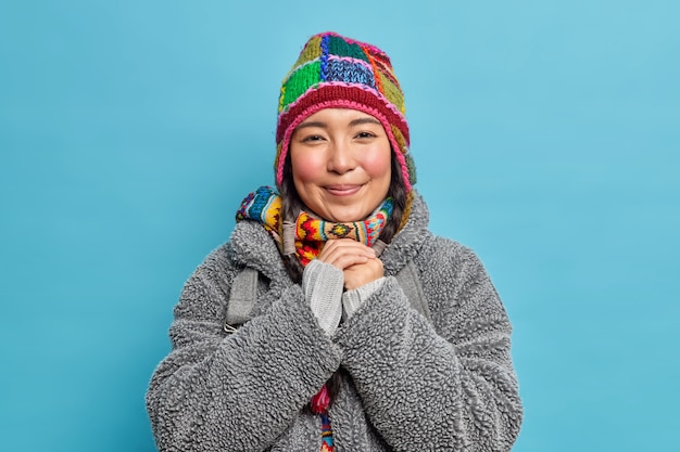 Foto gratuita la encantadora mujer esquimal con mejillas rosadas mantiene las manos juntas y sonríe agradablemente vestida con un gorro de abrigo y un abrigo de invierno de moda vive en un lugar ártico o en el polo norte