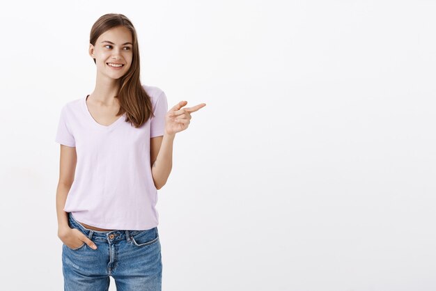 Encantadora mujer europea de aspecto amistoso en traje casual riendo amistosamente con una sonrisa mirando y apuntando hacia la derecha sintiéndose encantado