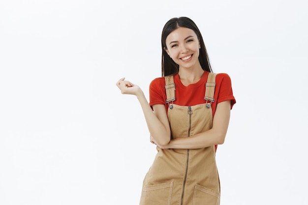 Encantadora mujer europea divertida y feliz en monos lindos sobre camiseta roja inclinando la cabeza riendo alegremente