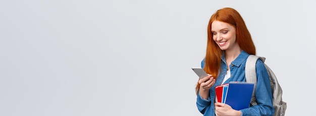 Foto gratuita encantadora mujer guapa con cabello rojo que se dirige a la universidad sosteniendo cuadernos de mochila sonriendo como ans