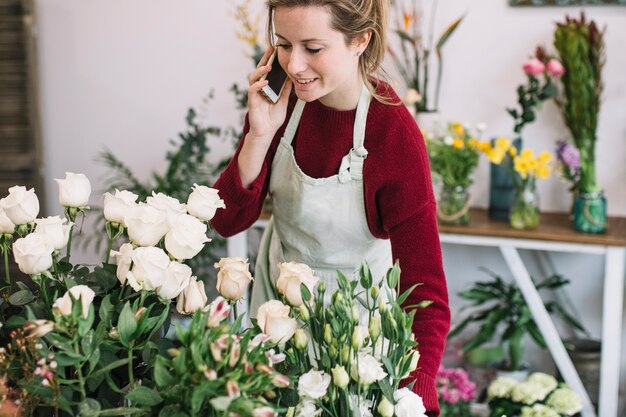 Encantadora mujer hablando en el teléfono inteligente cerca de las flores