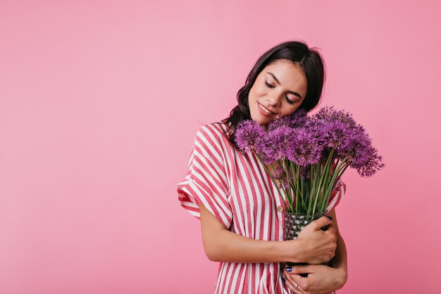 Encantadora mujer italiana de buen humor posa con flores de color púrpura.