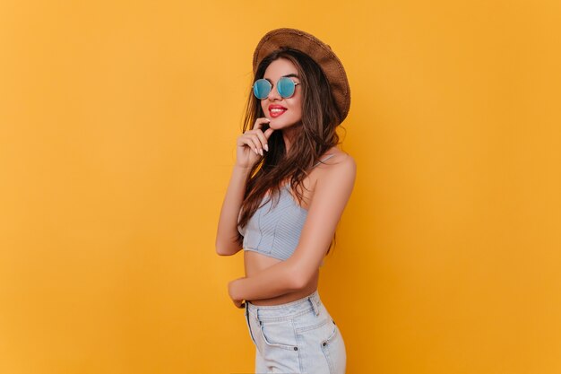 Encantadora mujer joven en elegantes gafas brillantes posando en el espacio amarillo