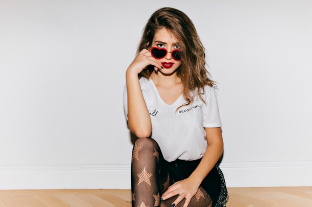 Foto gratuita encantadora mujer joven en gafas divertidas sentadas en el suelo