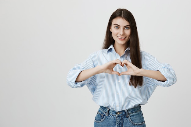 Encantadora mujer joven mostrando el signo del corazón y sonriendo