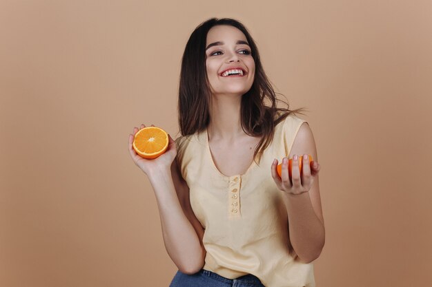 Encantadora mujer joven con una naranja sonríe posando en el estudio;