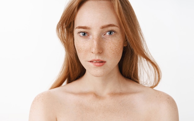 Foto gratuita encantadora mujer joven pelirroja femenina con pecas y hermosos ojos azules mordiendo el labio inferior por deseo e interés, volviendo la atención a lo intrigante que está parado desnudo