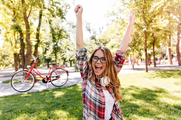 Foto gratuita encantadora mujer joven que expresa emociones emocionadas en el parque. alegre chica europea en camisa a cuadros escalofriante al aire libre.