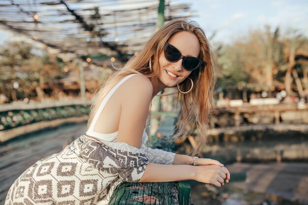 Encantadora mujer joven con sonrisa posando en la naturaleza. Tiro al aire libre de dama despreocupada ligeramente bronceada relajante en día de verano.