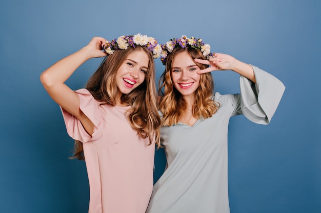 Encantadora mujer joven en traje rosa divirtiéndose con el mejor amigo en corona de flores