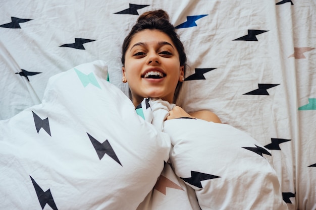 Encantadora mujer joven yace en la cama, cubierta con una manta