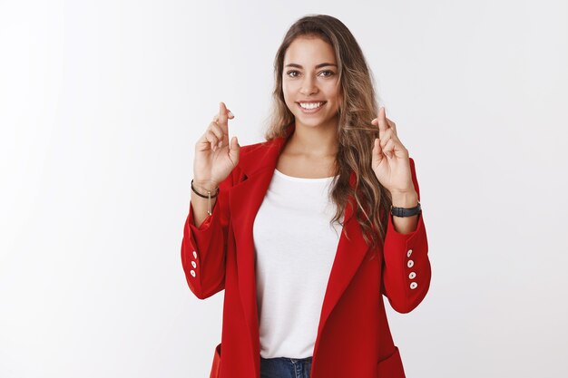 Encantadora mujer linda y afortunada, grandes esperanzas pasan la entrevista de trabajo con éxito cruzan los dedos para la buena suerte, con suerte sonriendo cámara rezando soñando anticipando resultados seguro de sí mismo, pared blanca