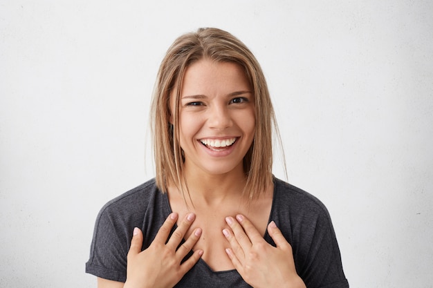 Encantadora mujer linda con peinado moderno y brillantes ojos marrones, sonriendo ampliamente, señalando a sí misma orgullosa de su éxito y victoria. Mujer sonriendo ampliamente con expresión agradable