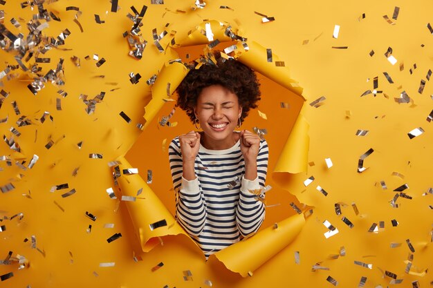 encantadora mujer linda se siente feliz, levanta las palmas de las manos, viste un suéter a rayas, expresa alegres emociones de ensueño