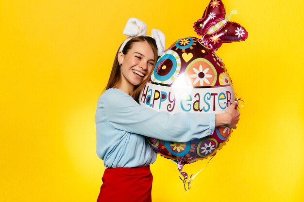 Encantadora mujer con orejas de conejo, abrazando globo de forma de huevo