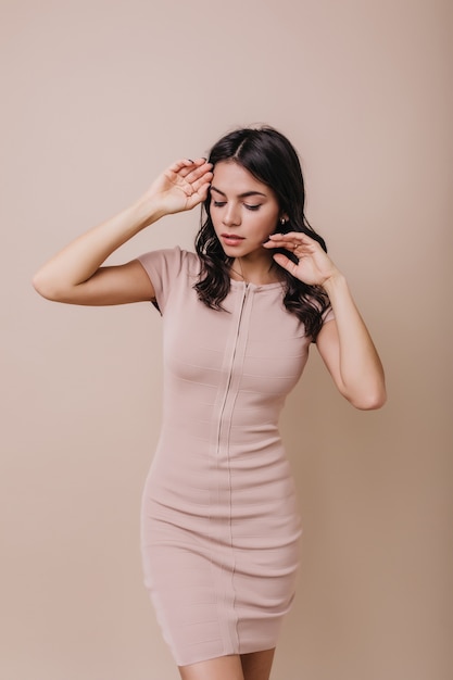 Encantadora mujer posando en vestido ajustado. El modelo de cabello oscuro mira hacia abajo, tocando suavemente la cara.