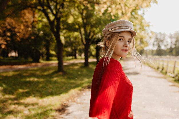 Encantadora mujer rubia mirando con encanto siguiendo a una persona en el parque de otoño.