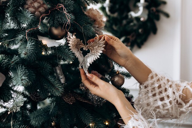 Encantadora mujer rubia con vestido blanco posa en una habitación con un gran árbol de Navidad