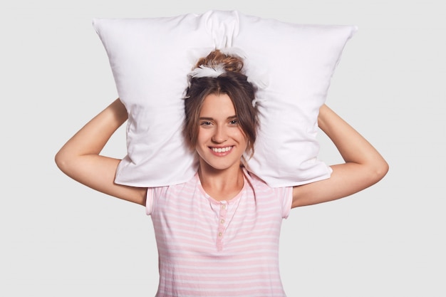 Foto gratuita encantadora mujer satisfecha con una sonrisa encantadora, mantiene la almohada detrás de la cabeza