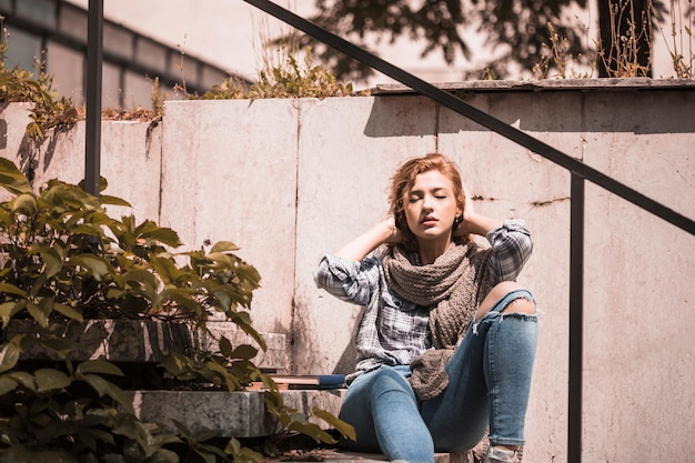 Encantadora mujer sentada en pasos cerca de libros y reajustar los pelos